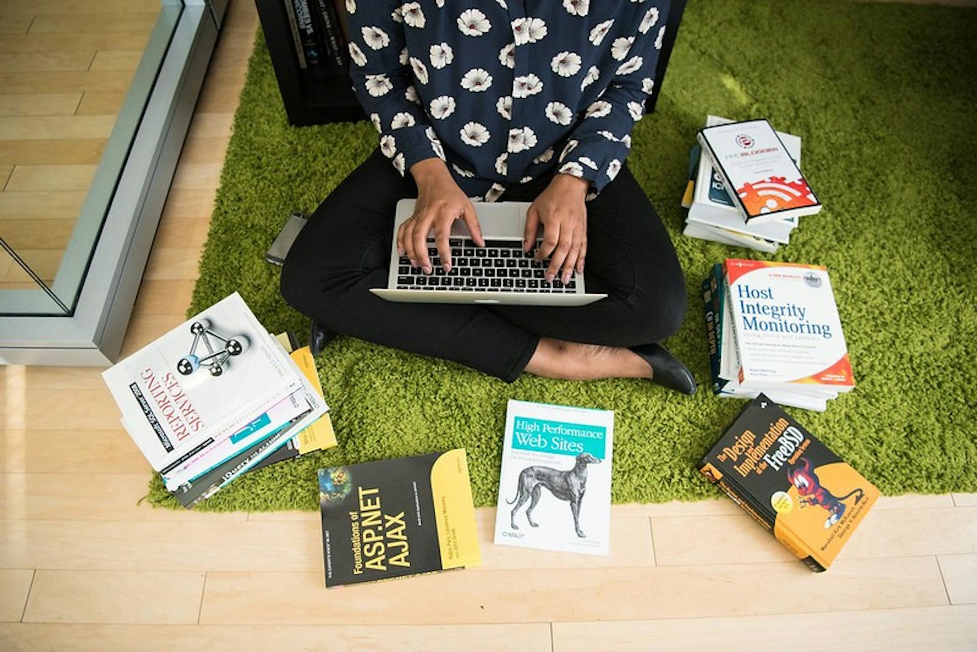 Pessoa com computador no colo e livros no chao