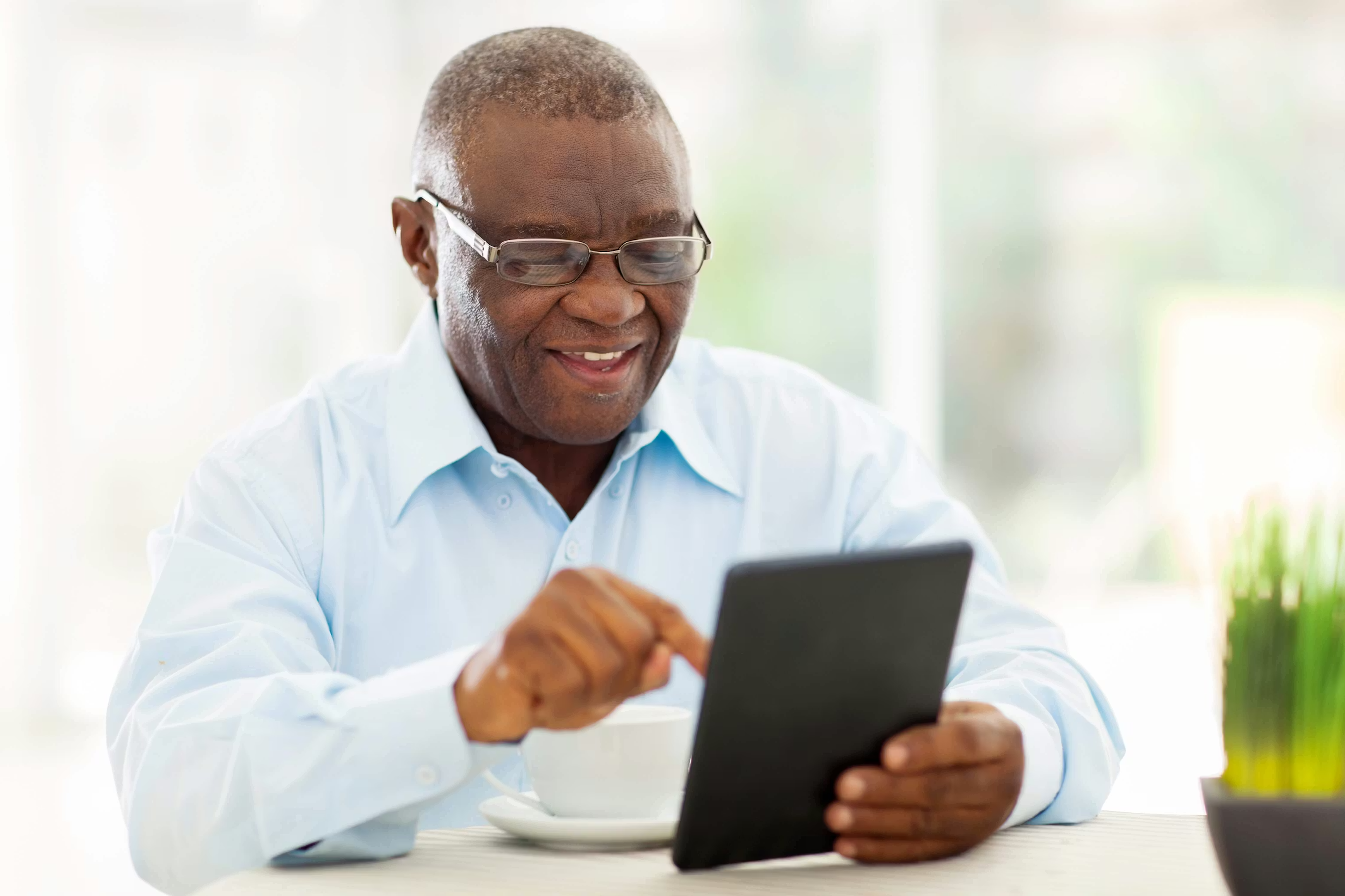 Smiling older man using a tablet at a table with a cup of coffee.