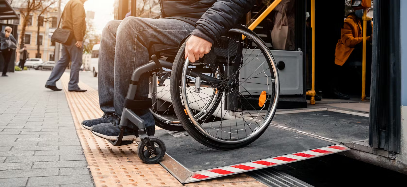 Wheelchair user entering a bus using a portable accessibility ramp at a curbside stop.