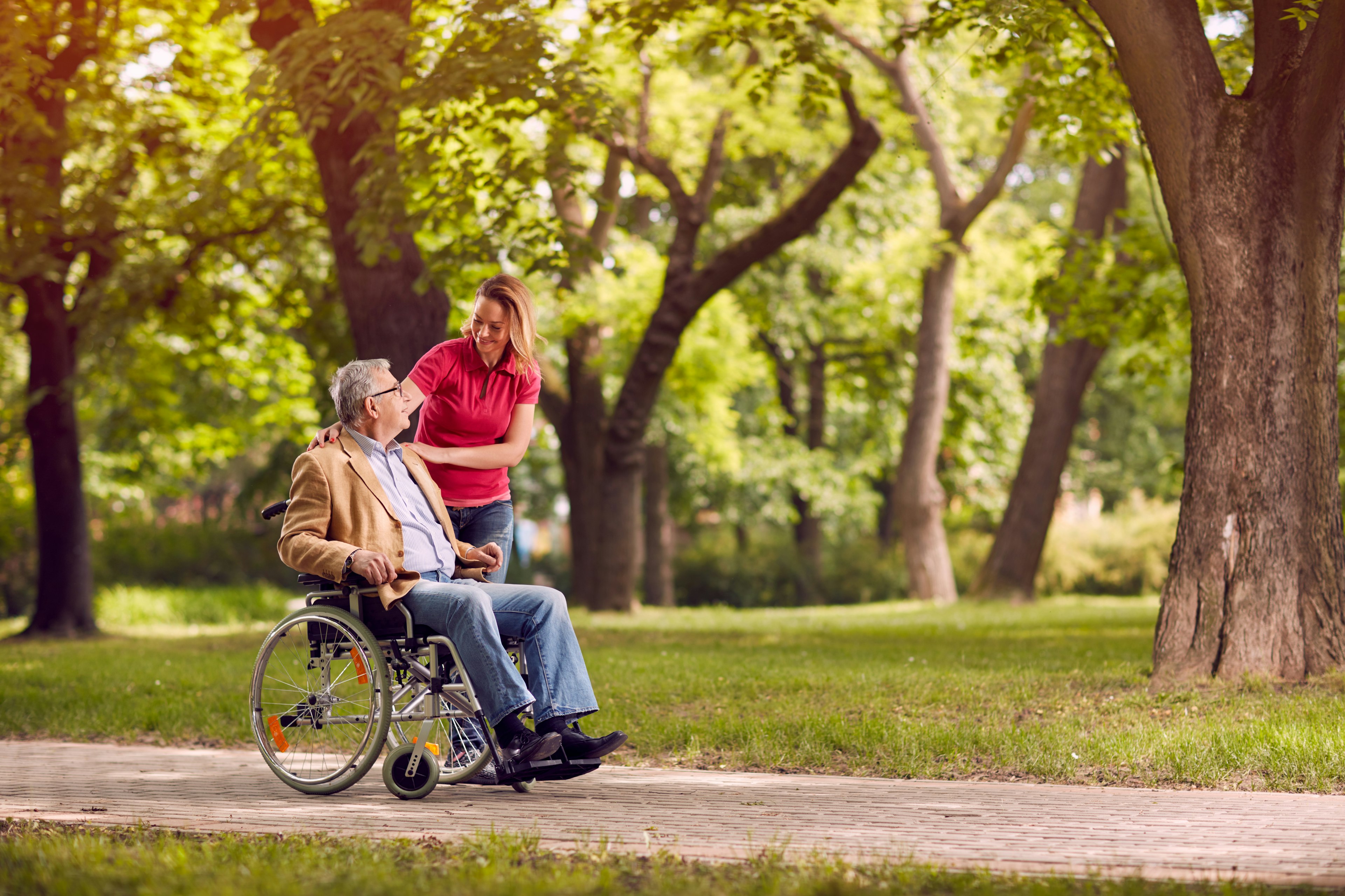 Happy senior man in wheelchair in the park with smiling daughter in the park