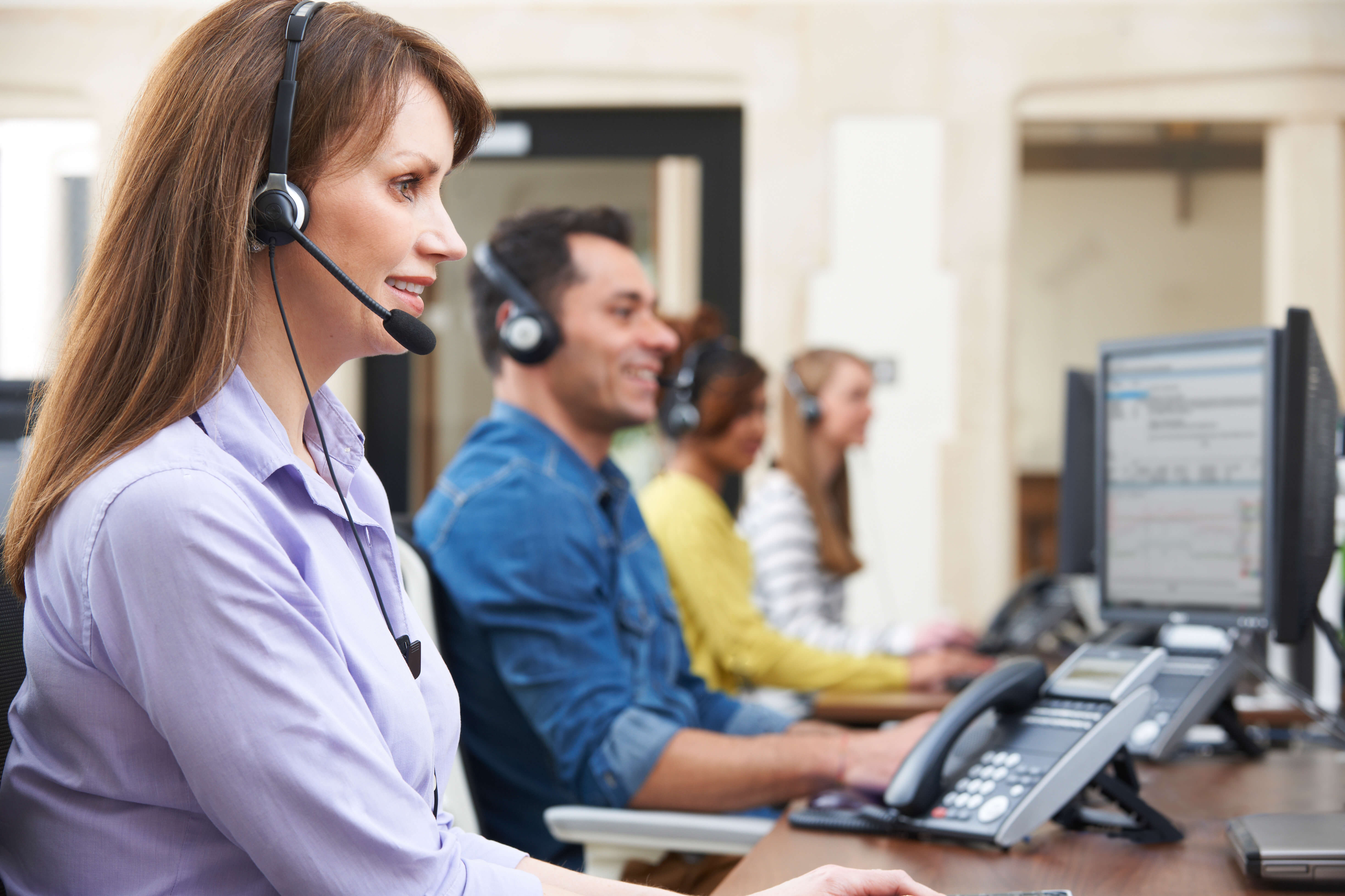 Call center agents wearing headsets and working at desktop computers.