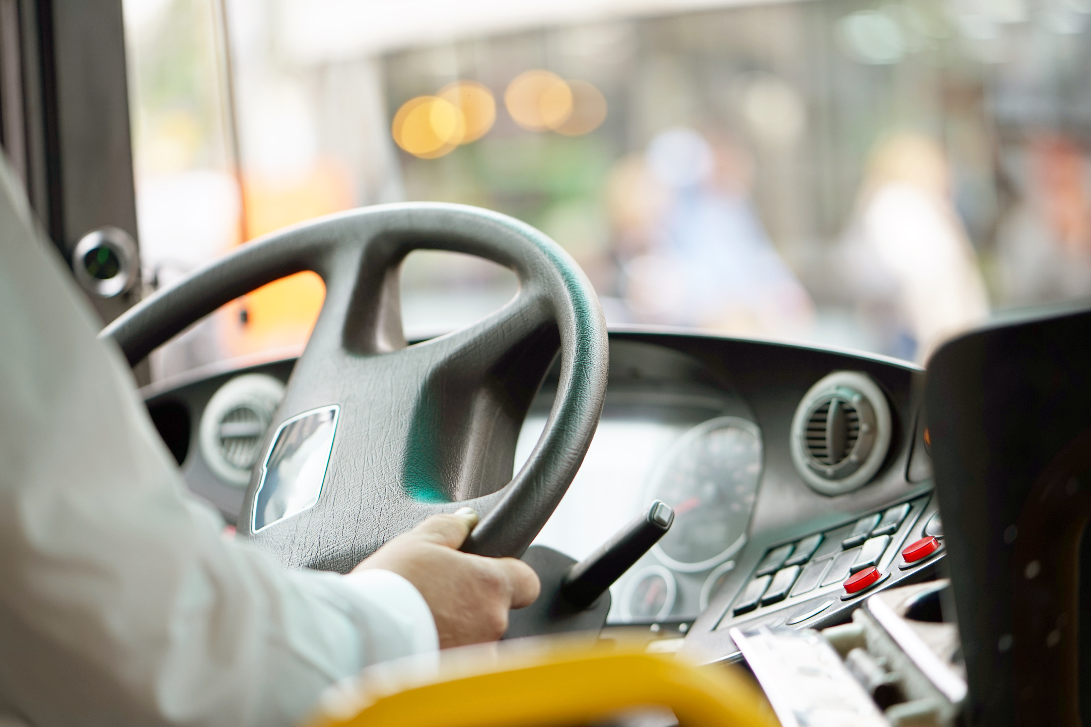 Close-up of a bus driver’s hands on the steering wheel inside the vehicle cab.