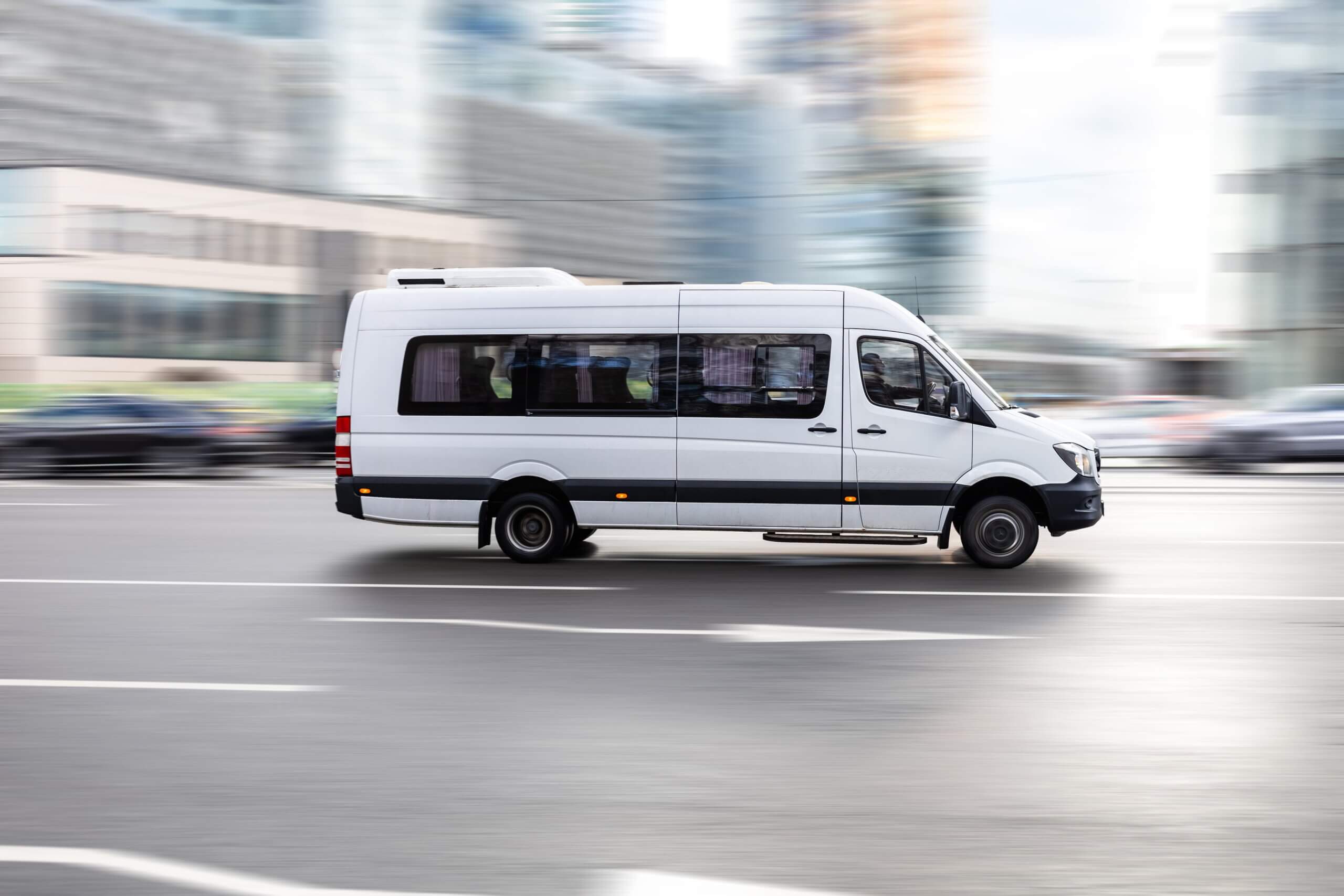 White passenger van driving quickly through a city street.