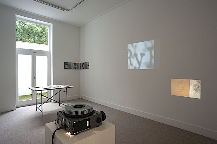 Vonna-Michell, Boxed Matter, 2022, table, plexiglass, printed matter from E.E. Vonna-Michell and Balsam Flex, 7 boxes with biodegradable elements, 120 x 80 cm (table), 18,3 x 18,3 cm (boxes, each); Tris Vonna-Michell, Broadway (after vonna-michell´s house by Henri Chopin, 1985), 2021, digital inkjet prints, diptych (each part: 32 cm x 76 cm); E.E. Vonna-Michell and Henri Chopin, To Ray The Rays, 1986-87, 16mm film transferred to video, sound, colour, 7 minutes 55 seconds; Tris Vonna-Michell, back segments, 2022, slide projection, 35 colour slides (35mm), audio, back segments publication by E.E. Vonna-Michell, 8 minutes 03 seconds. Installation view of Vonna-Michell: back segments at Jan Mot, Brussels, 2022, from back to front, left to right