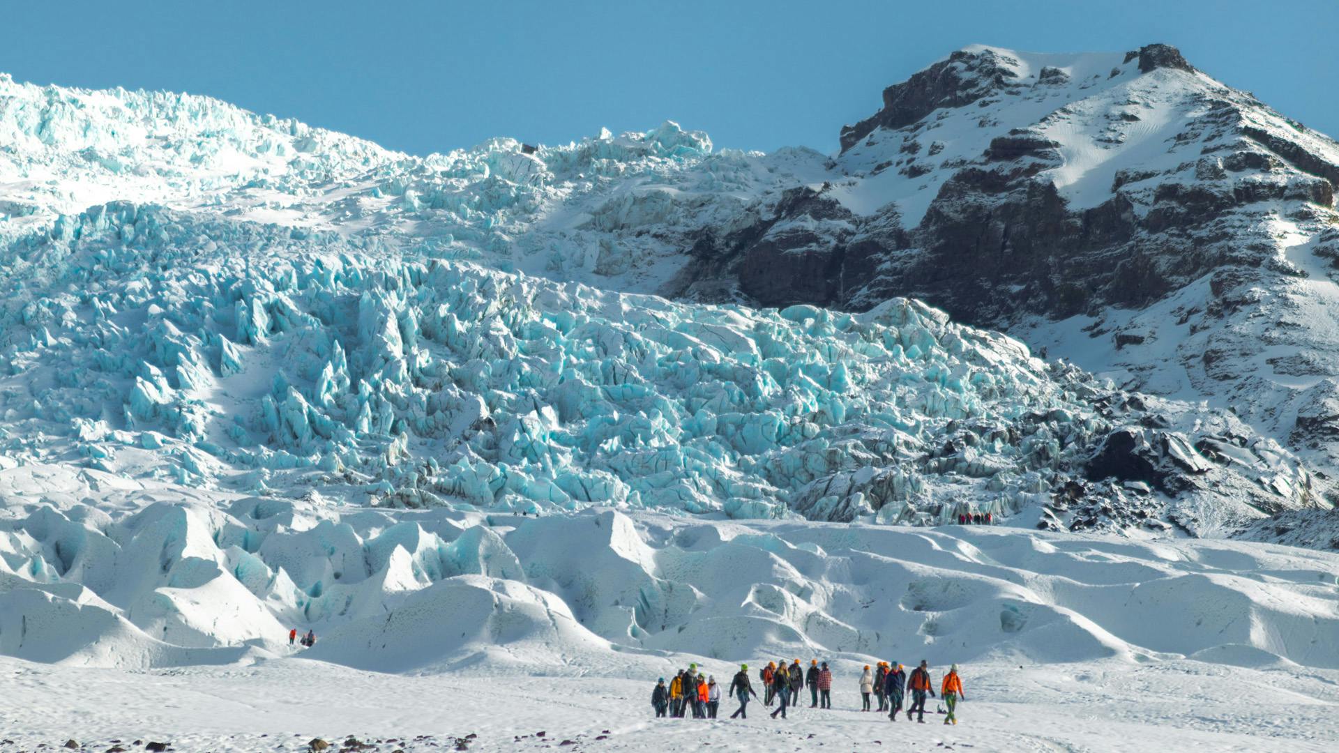 A group of people walking on a glacier plateau.