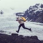 A man running and jumping between rocks with a glacier on the background.