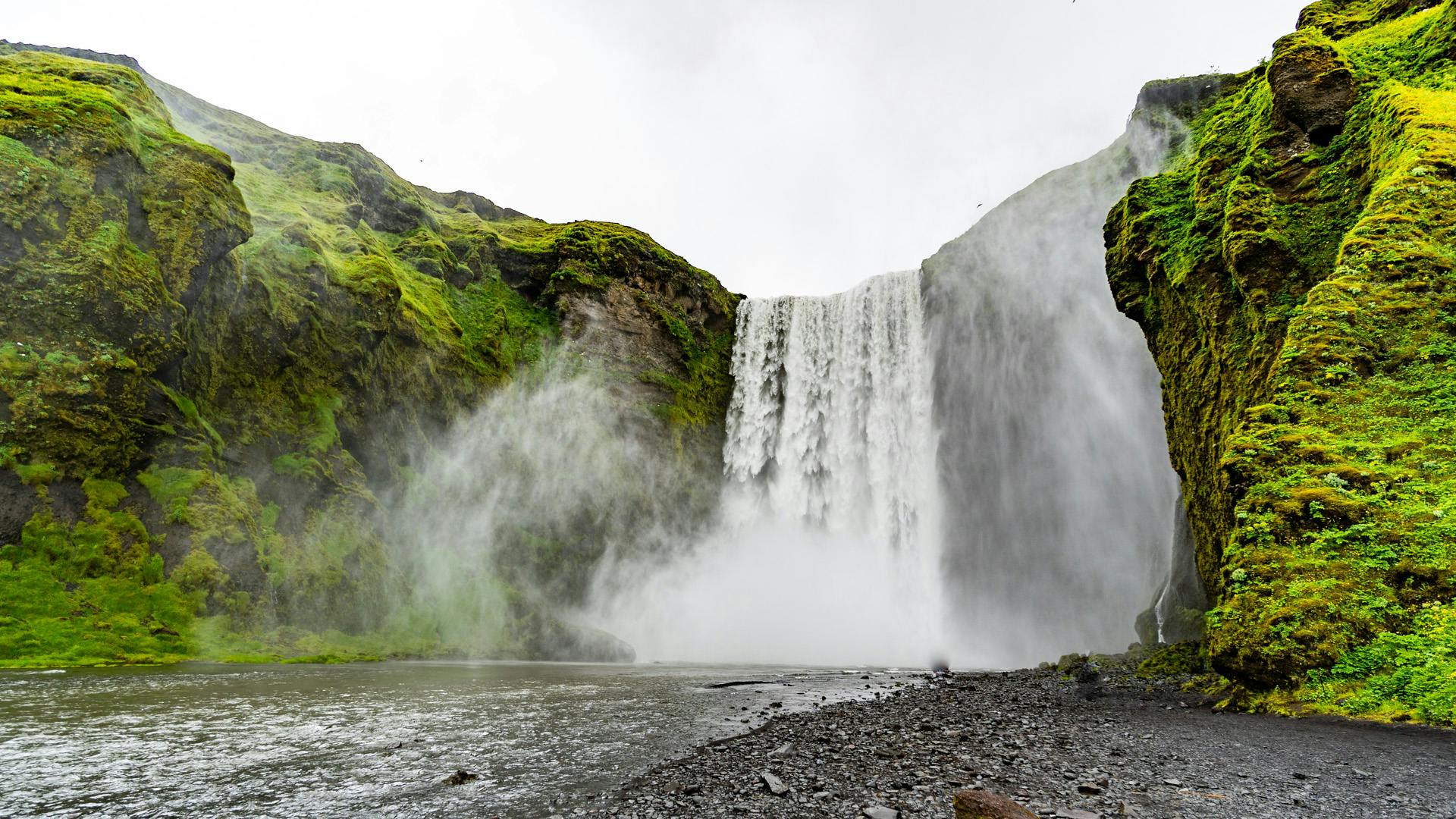 Waterfall with a lot of mist flying around the canyon, and the wall of the canyon is covered with moss.