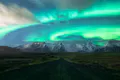 Road leading to the mountains with aurora borealis lightning up the sky.