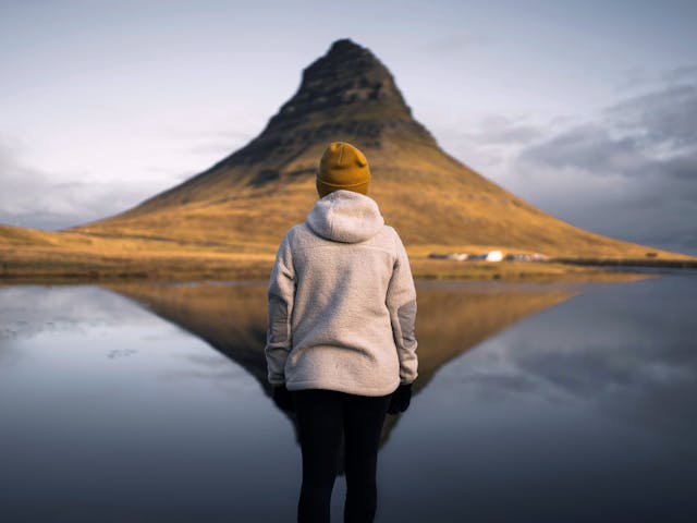 Person photographed from the back wearing a wool jacket and beanie with a pyramid shaped mountain in the background.