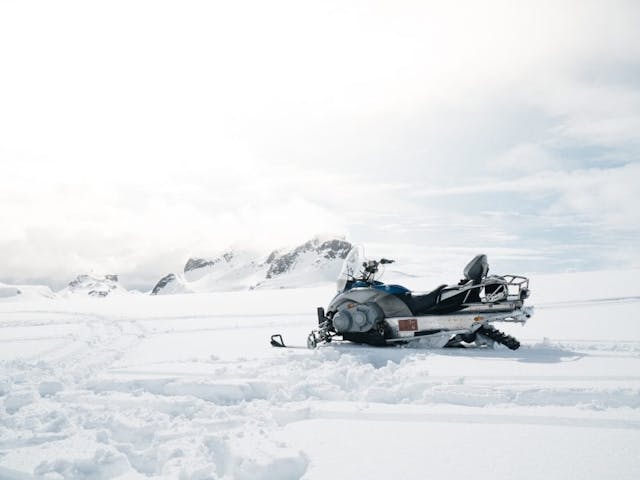 An empty snowmobile on the Glacier Langjökull surrounded with snow with a view of a cliff in the background.