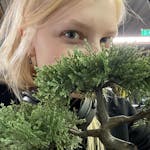 A blonde girl with a bonsai covering half of her face.