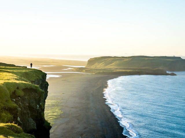 Person standing near a cliff while photographing the landscape during summer time.