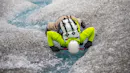 A person in a green jacket is drinking water directly from a glacial stream.