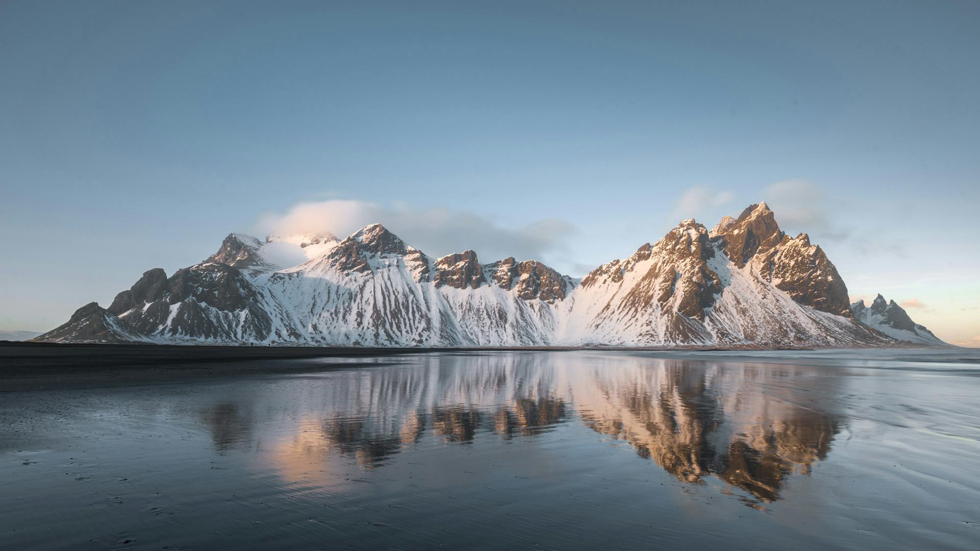 Vestrahorn mountain covered with snow while the shallow and calm beach is creating a gorgeous reflection in the water.