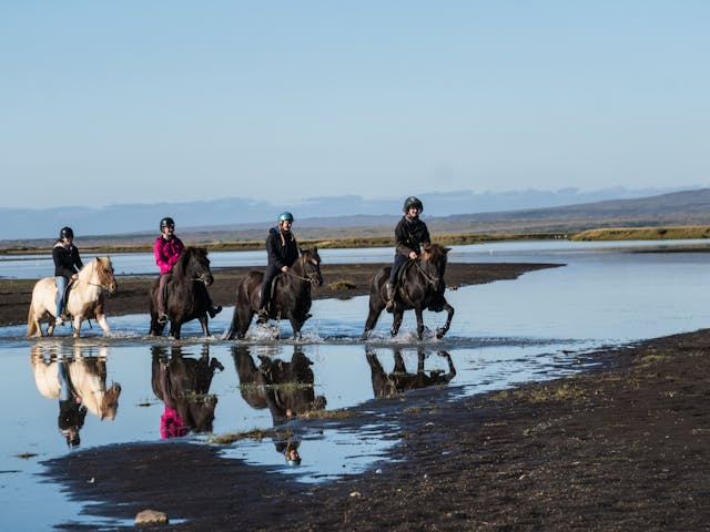 People are riding horses over a river.