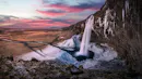 Huge waterfall on a ridge with stalactites of ice and snow on the side walls and floor.