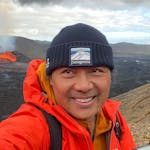 profile picture of a person using a red jacker and a hat with a volcano on the background