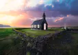 Small stone walls with a black church inside the perimeter, a colorful sunset is striking in background.