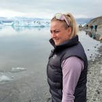 A blonde girl with glasses standing next to glacier lagoon