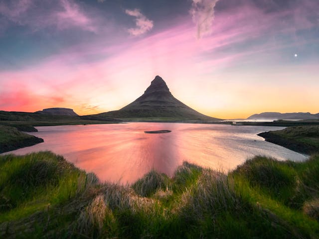 Pyramid shaped mountain on the far side of the lake with sunset colors all around.
