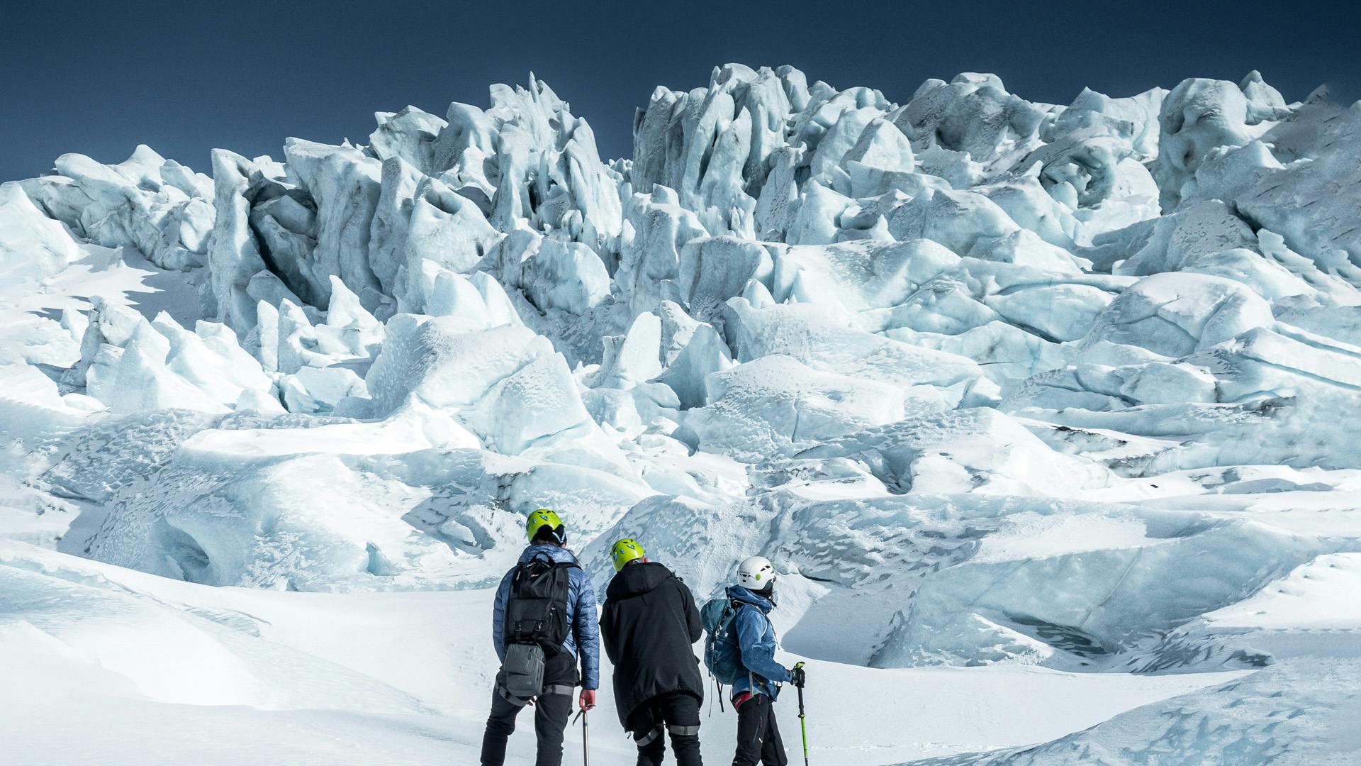 Three people watching the ice falls on a glacier.