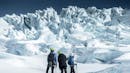 Three people watching the ice falls on a glacier.