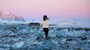 Woman running between chunks of ice on a black sand beach.