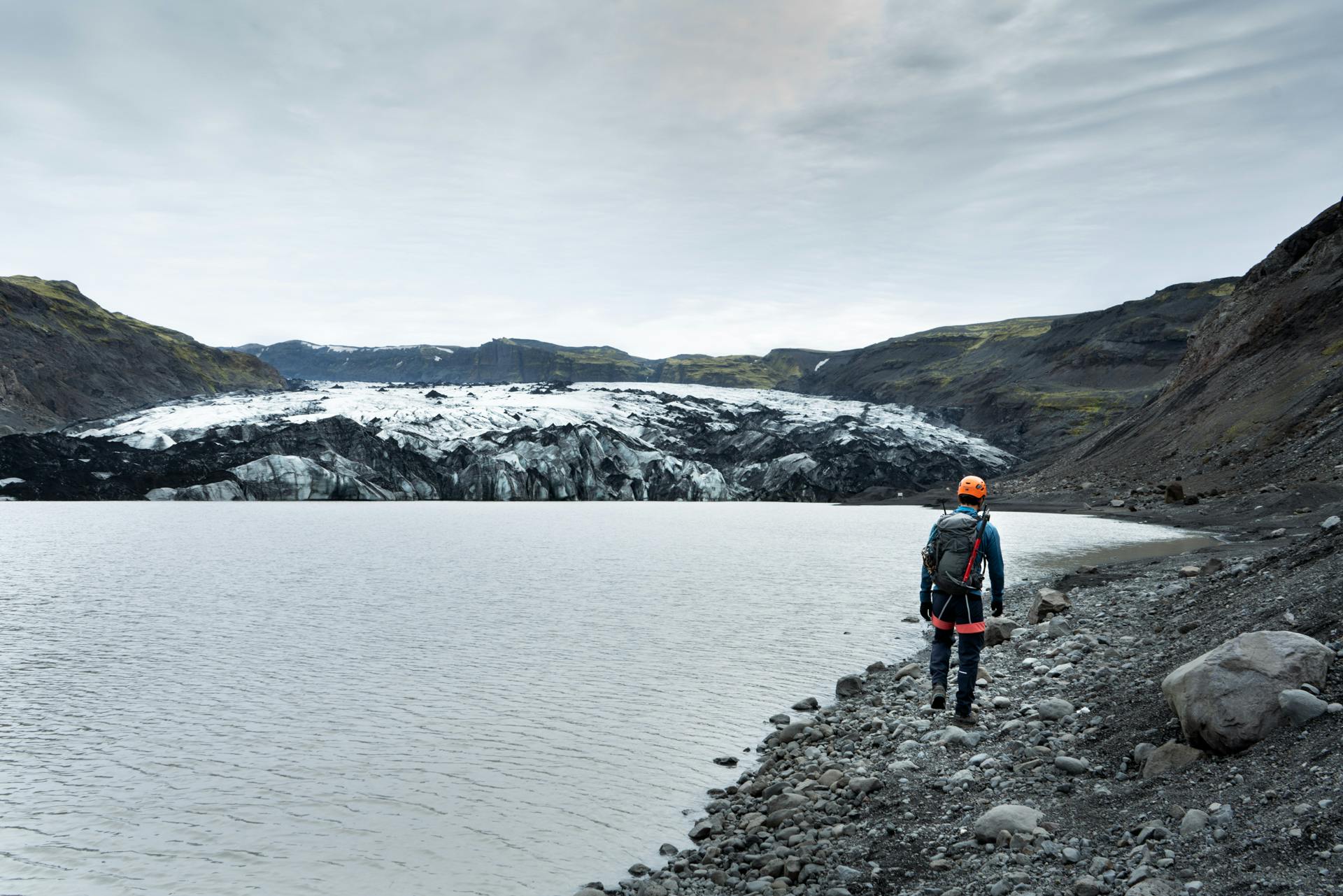 Person walking along the lagoon with a glacier in the other side of the lagoon.