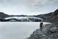 Person walking along the lagoon with a glacier in the other side of the lagoon.