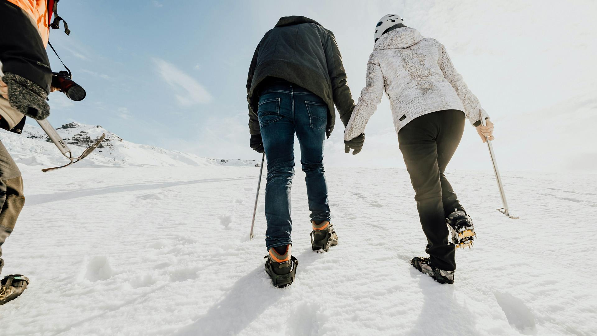 Couple holding hands and hiking on a glacier.