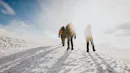 Three people walking on a glacier with the sun bursting.