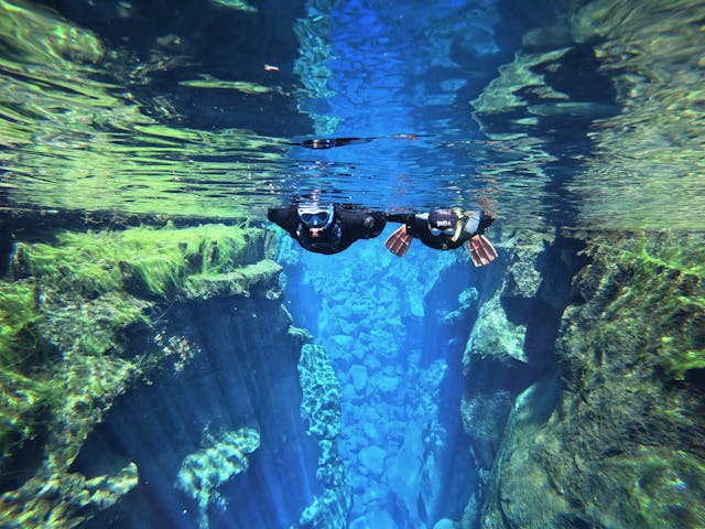 Two people snorkeling on translucent glacial water between a tectonic fissure.