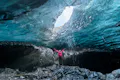 A woman wearing a pink jacket with her arms wide open looking at the ceiling of an ice cave.