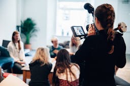Person using a camera to video a group of people talking around a table