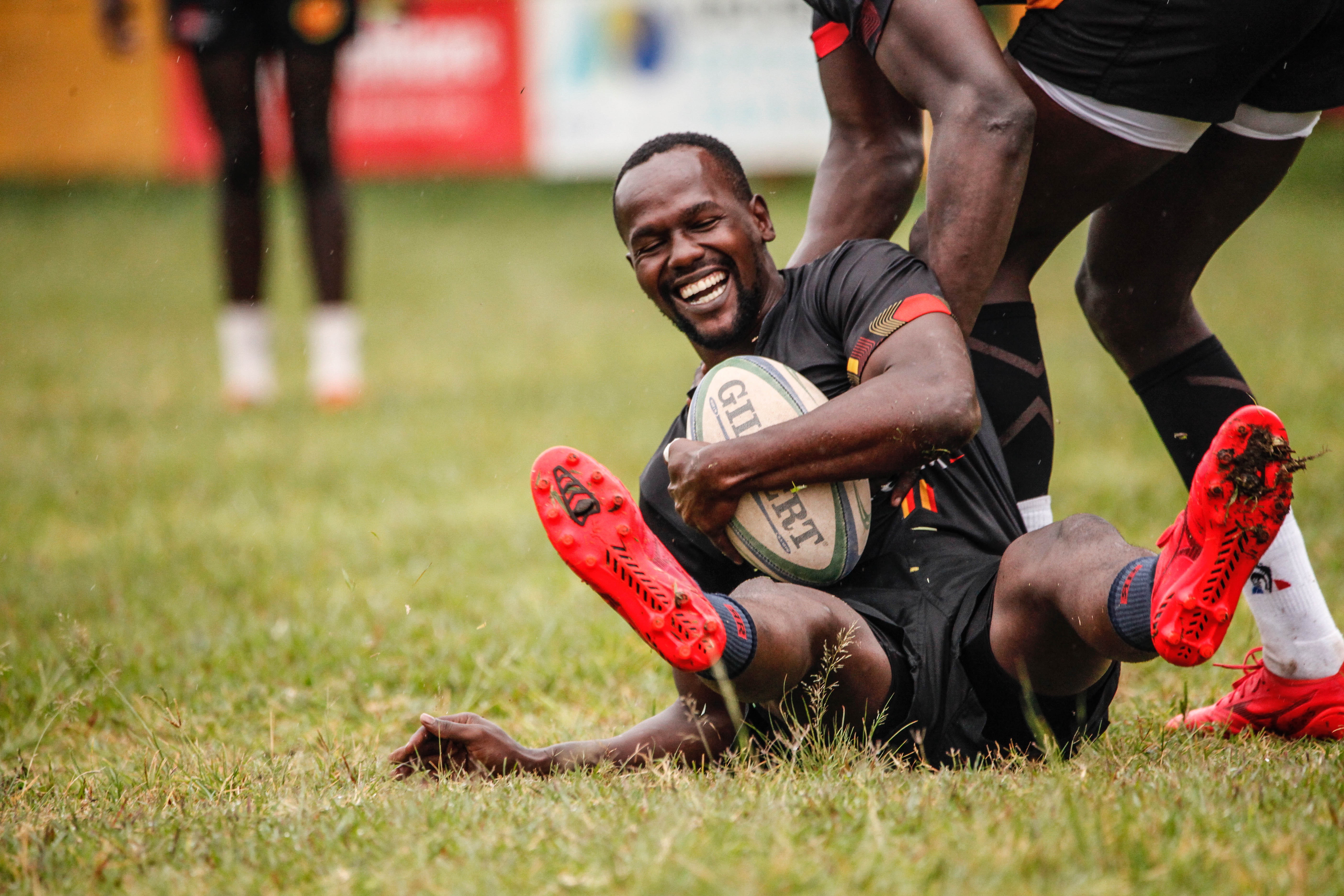 Smiling Rugby player holding ball across chest being helped up off the floor by teammate