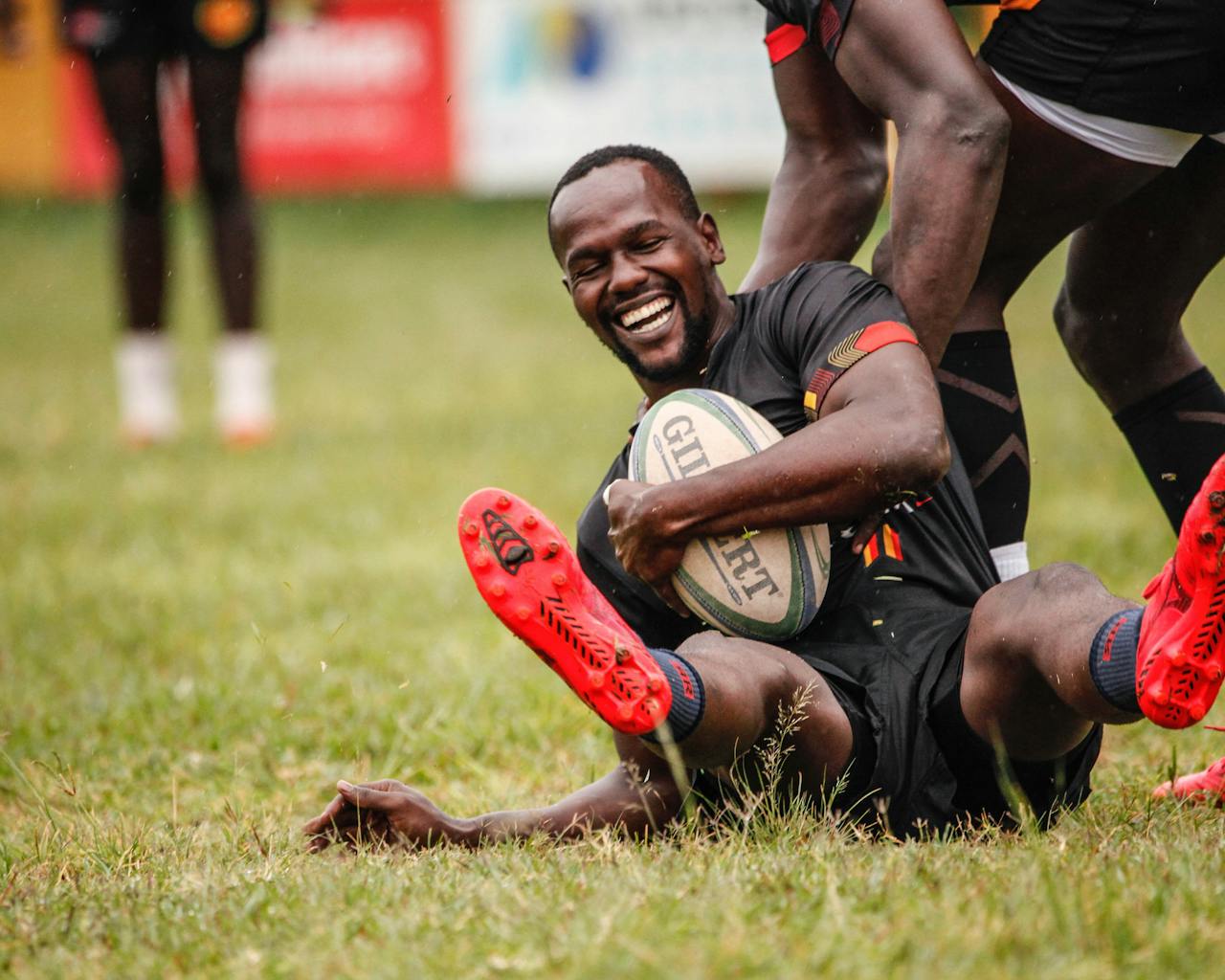 Smiling Rugby player holding ball across chest being helped up off the floor by teammate
