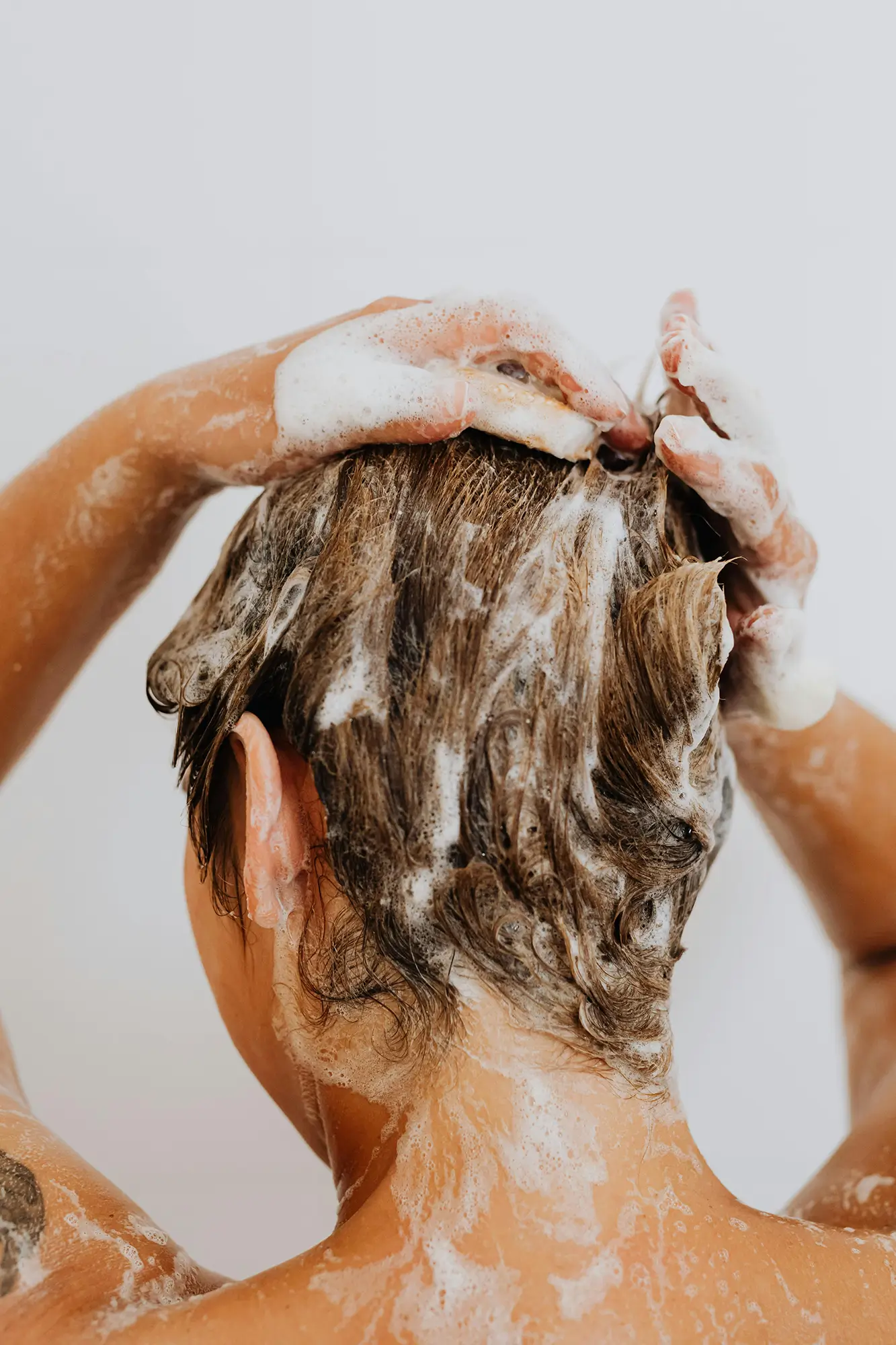 White person shampooing their hair against a white background