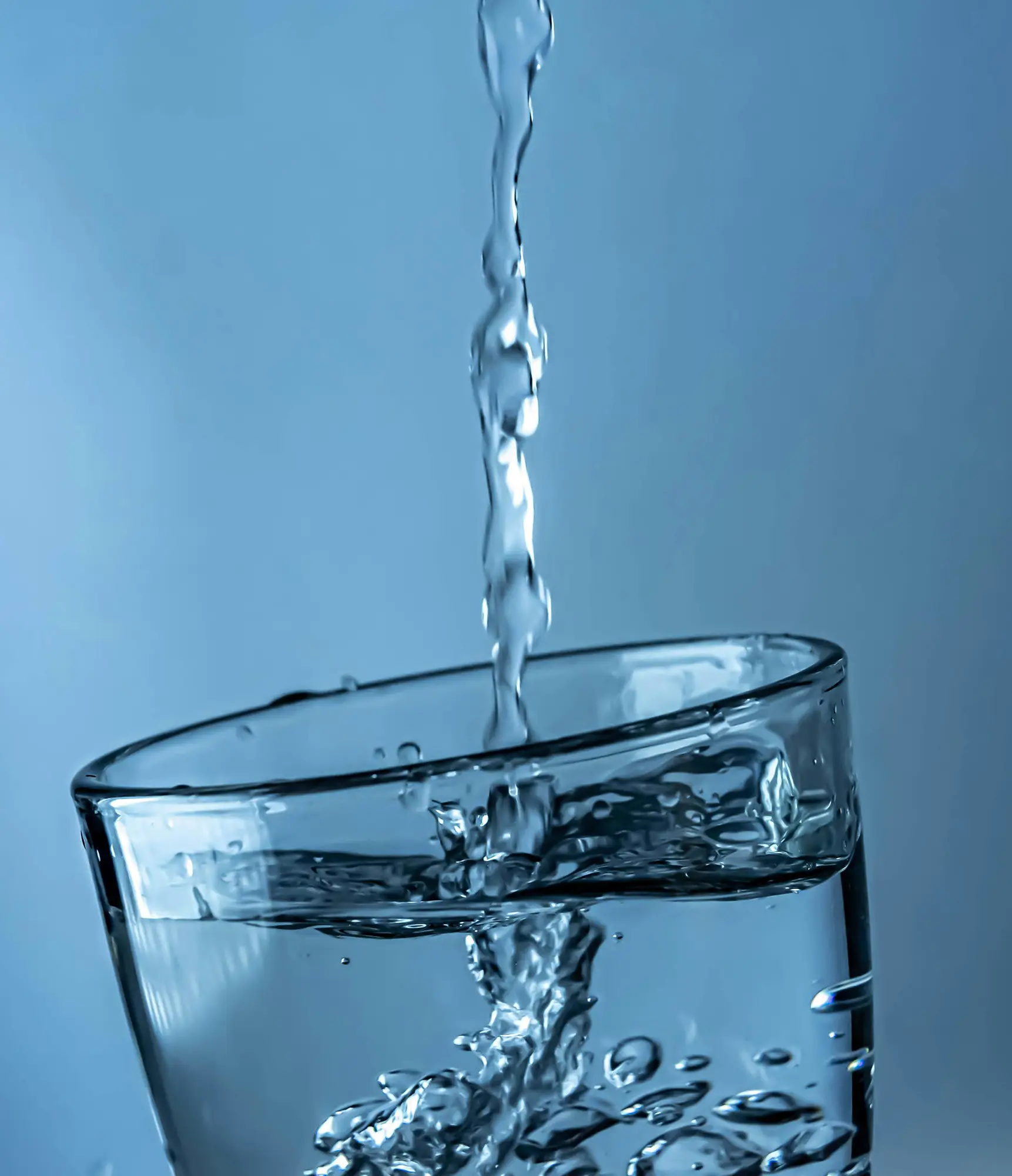 Closeup of water filling a crystal clear glass against a soft blue background