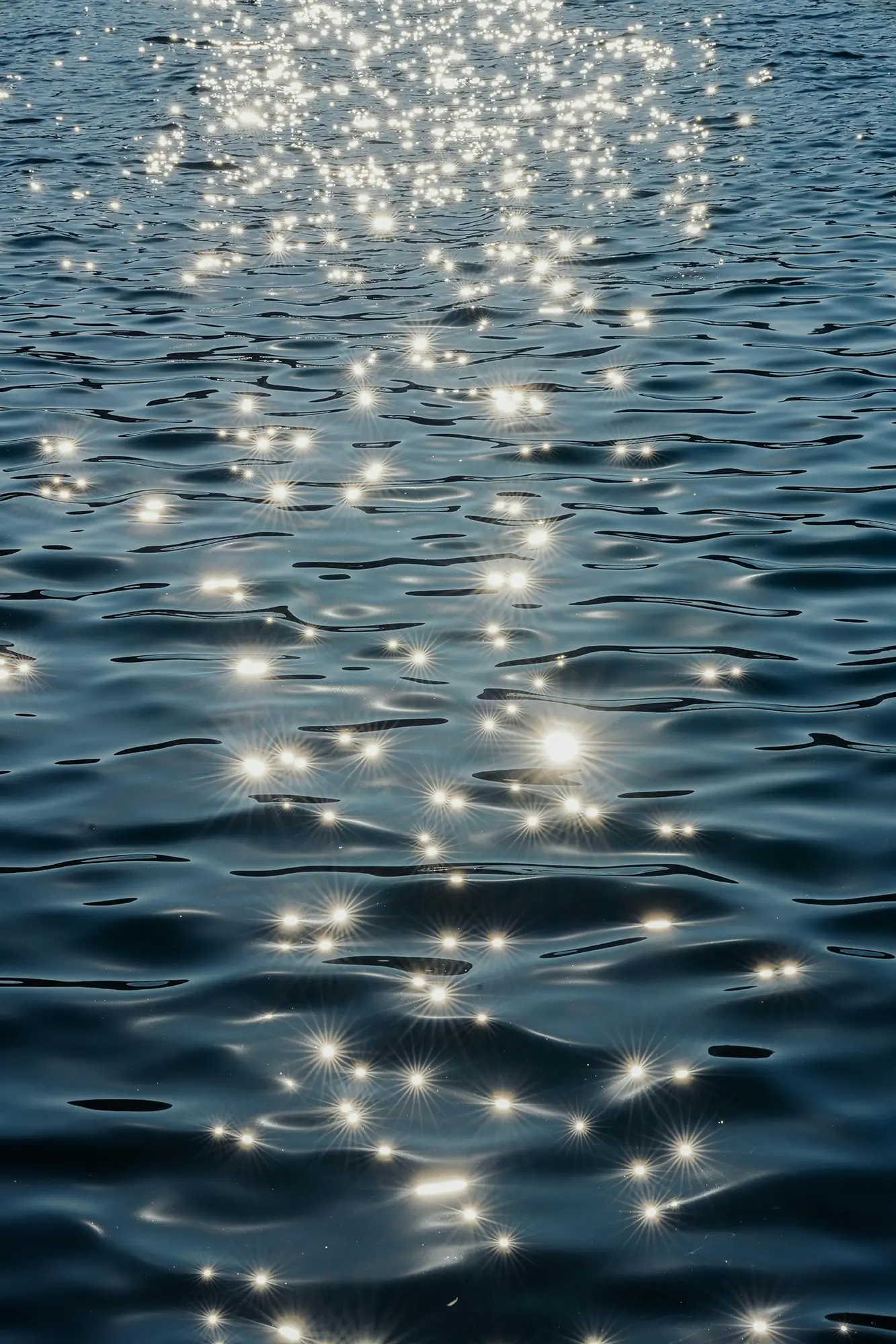Calm blue water covered in bright spots of reflected sunlight