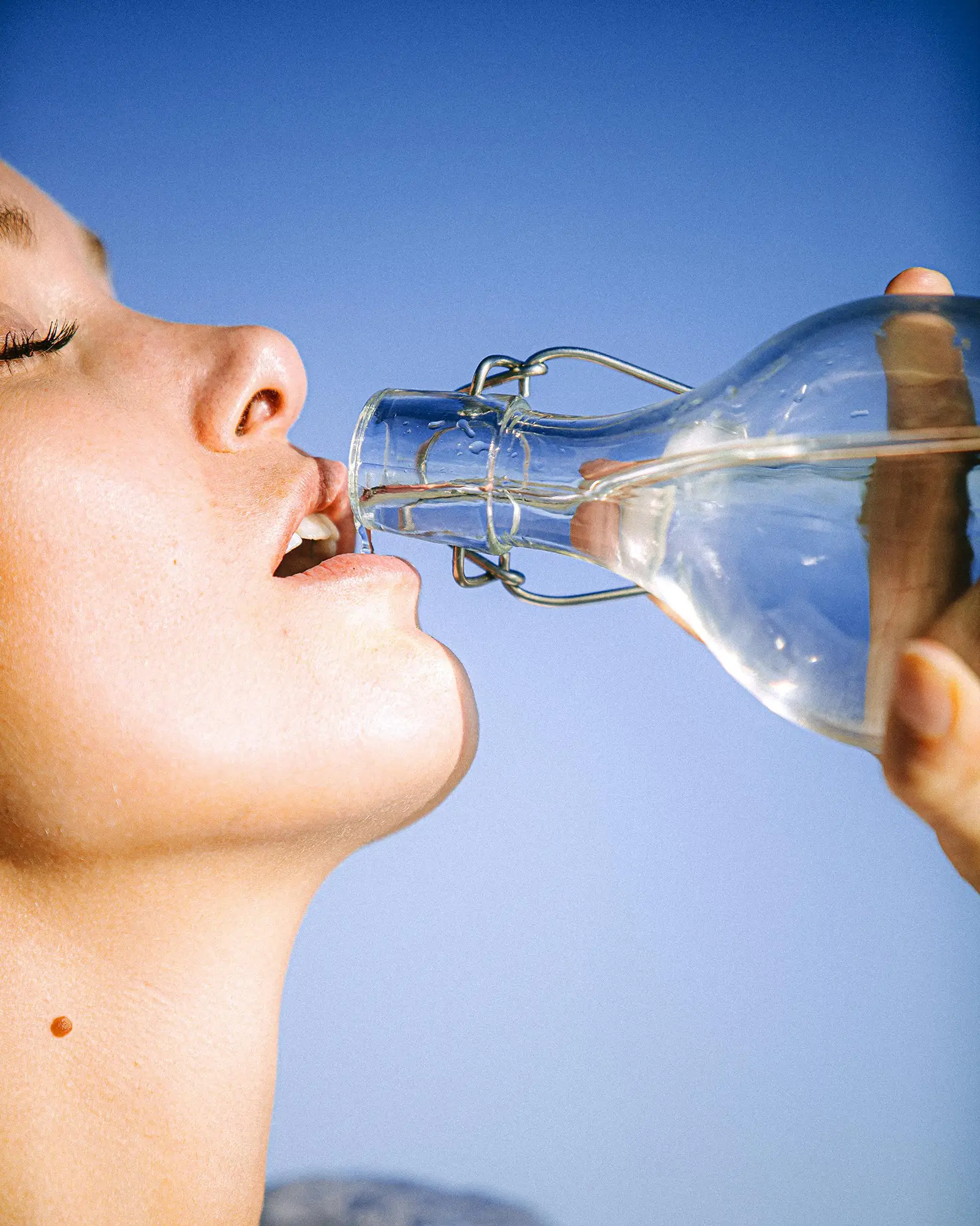 Closeup of a young white woman drinking water against a blue gradient background