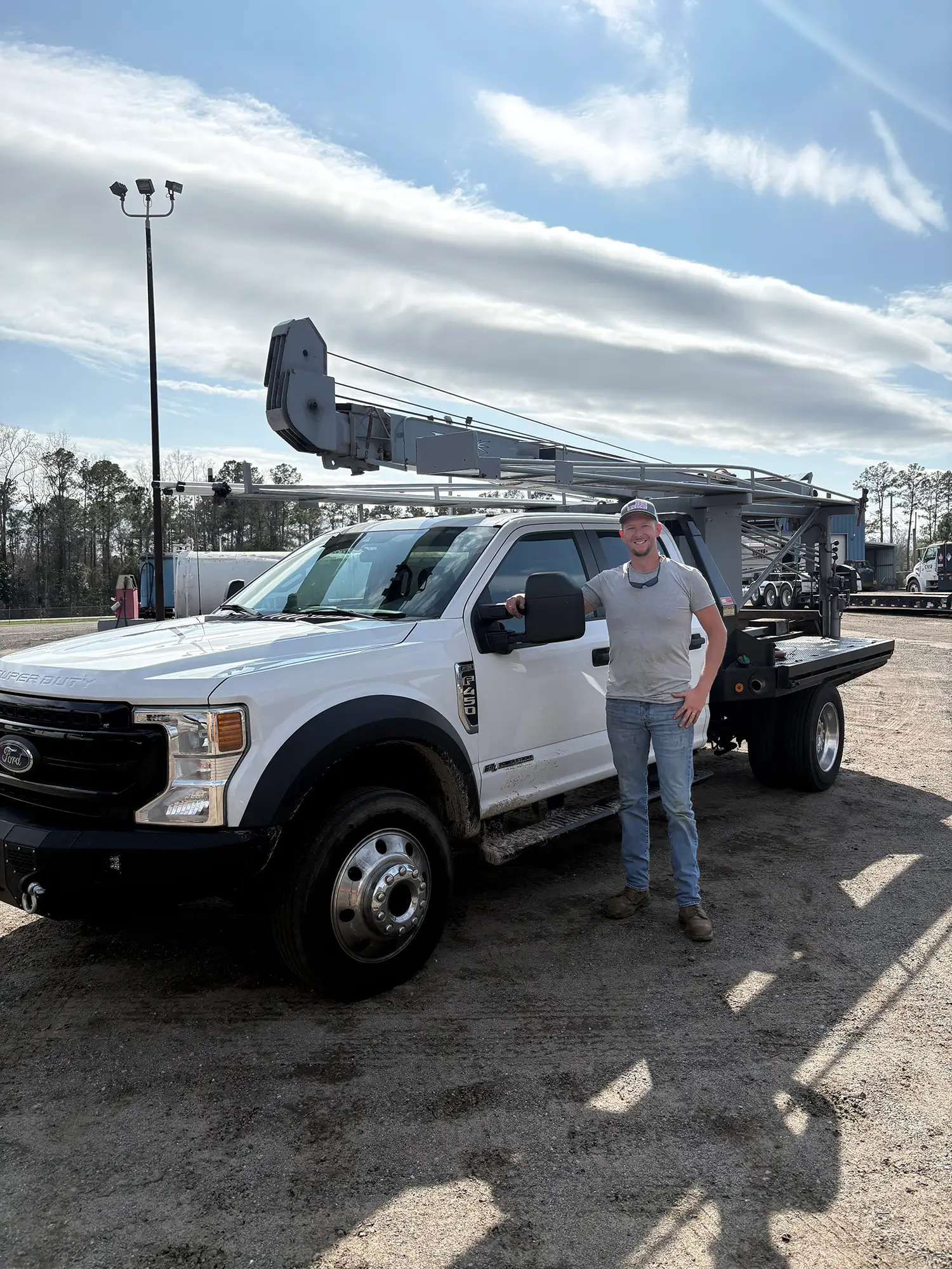 Man in a t-shirt, jeans, and American flag ball cap standing in front of a large white pickup truck