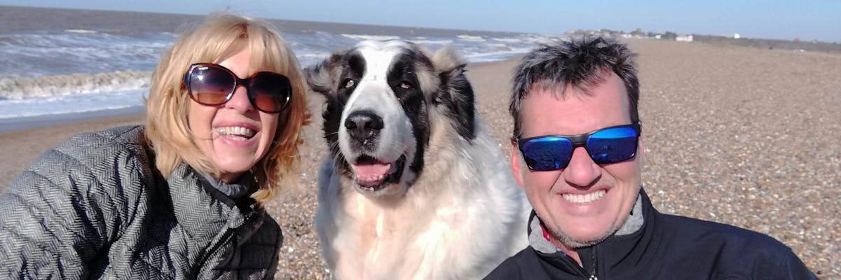 A woman, a man, and a dog smiling at the camera on the beach
