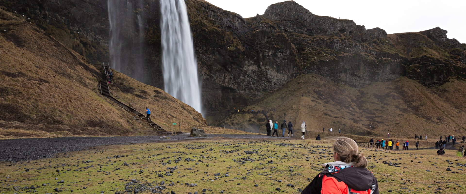 solo female traveler looking at a huge waterfall in Iceland surrounded by black volcanic hills