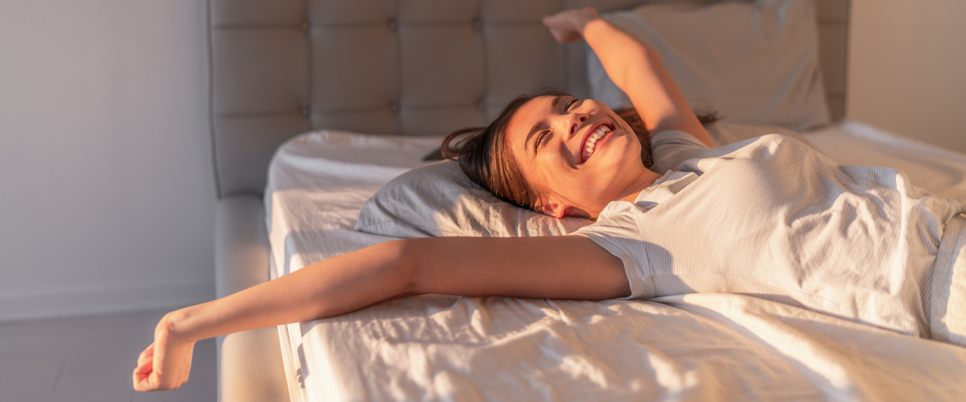 A solo female traveler stretches her arms out on a bed.