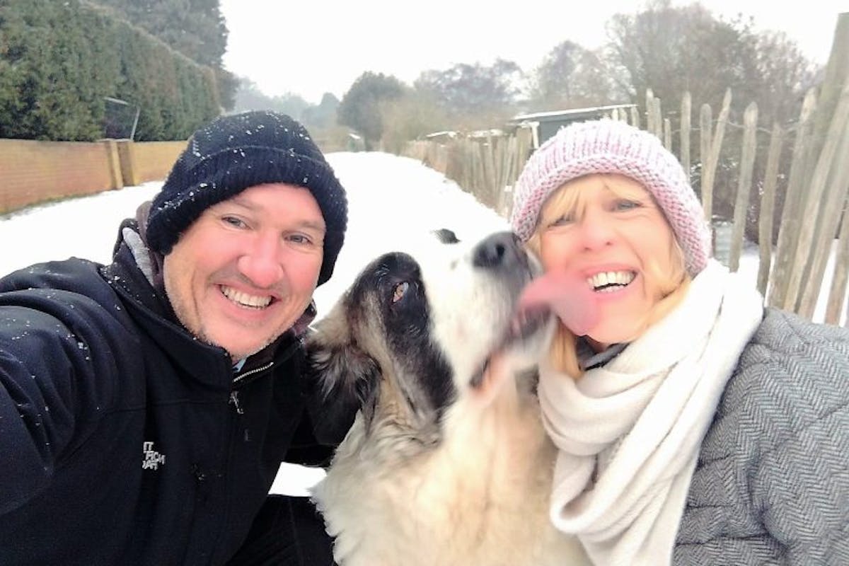 A man and a woman smiling at the camera, while a dog licks the woman's face