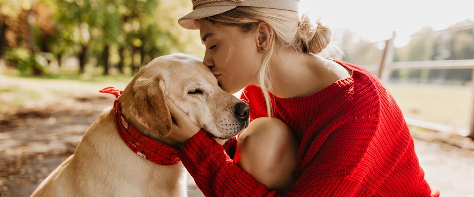 A woman wearing a bright red jumper kissing her dog on the top of the head