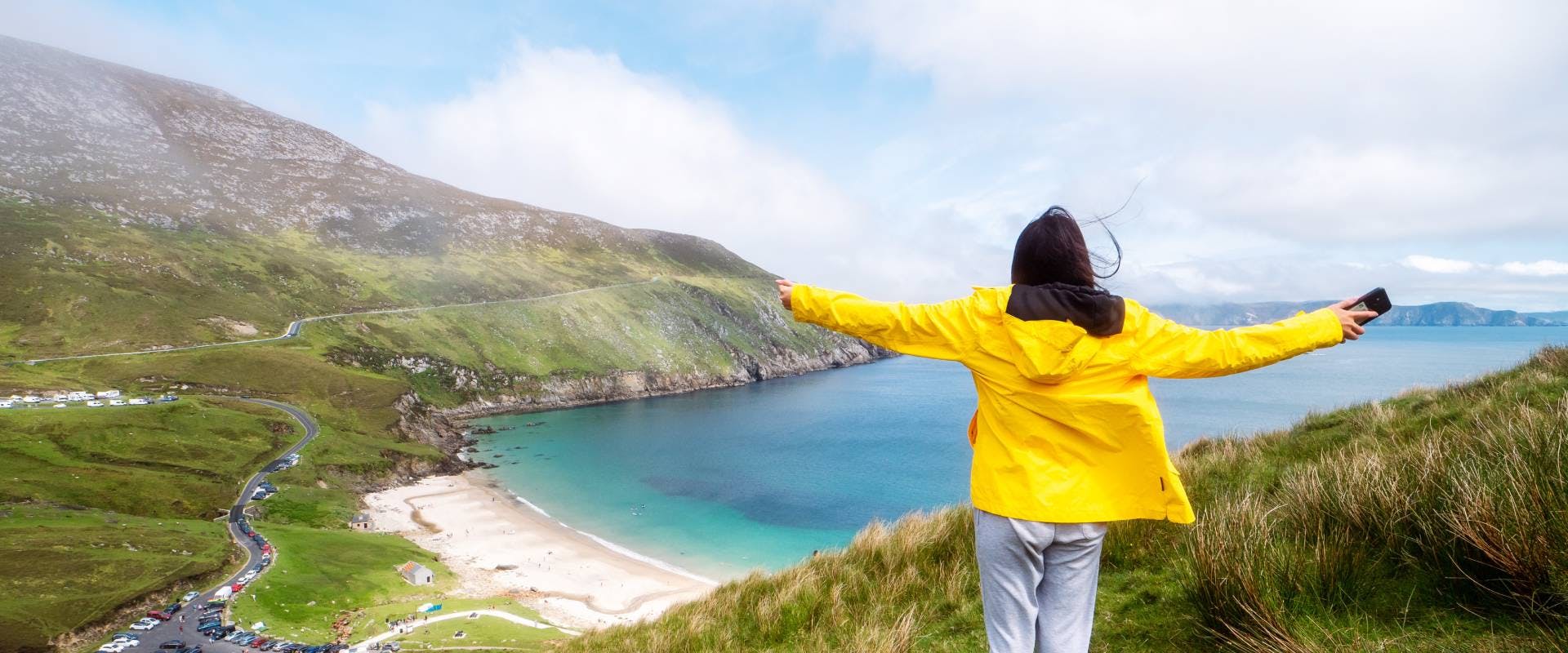 solo female traveler in a yellow rain coat looking out over an irish beach