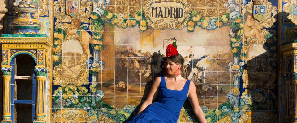 A flamenco dancer sits in front of a tile wall.