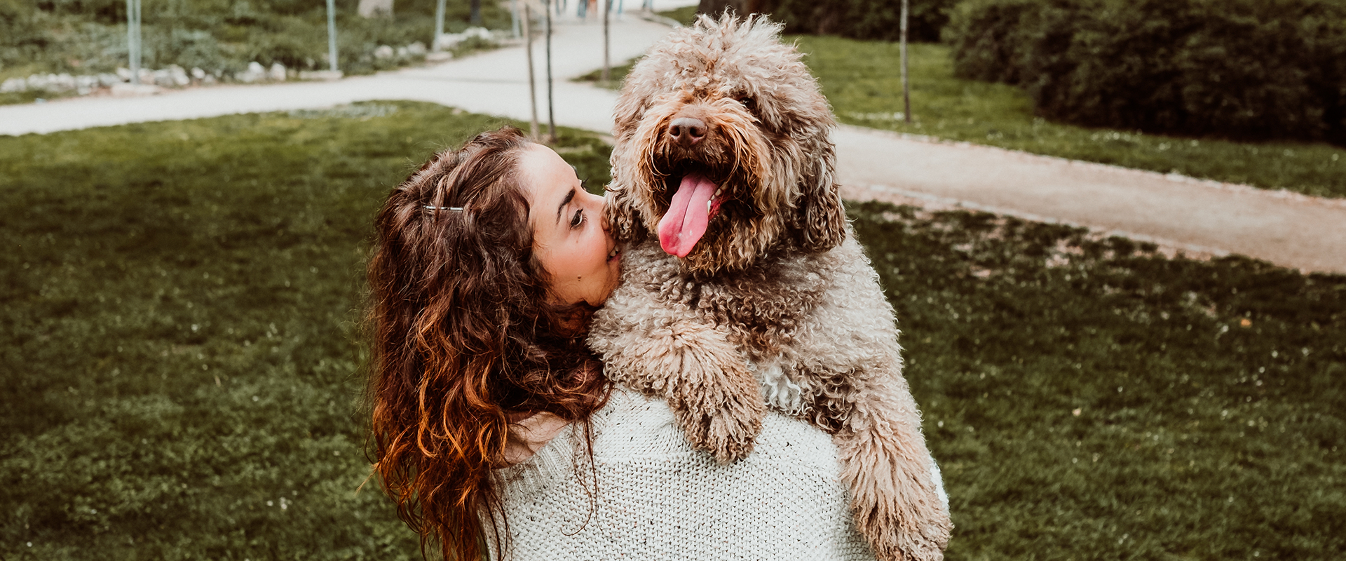 A woman holding a dog in her arms in the middle of a dog park