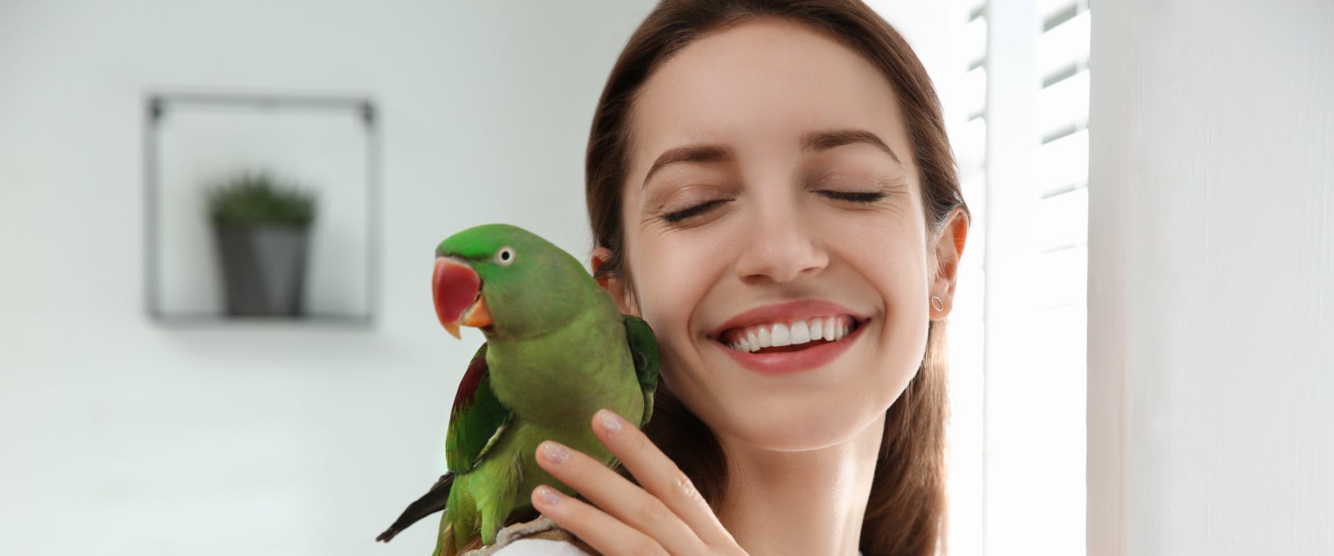 a smiling woman with a green parakeet on her on her shoulder